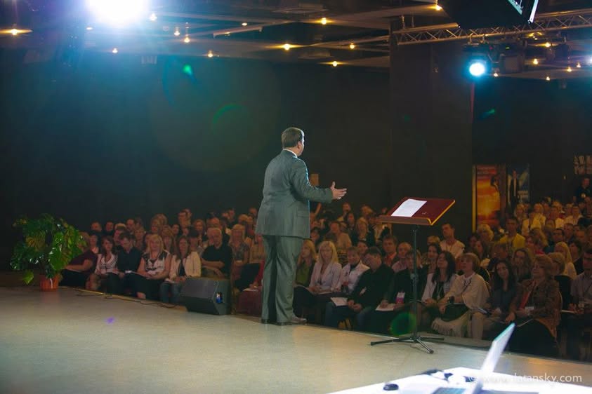 Mykola Latansky addressing a seated audience from the stage in Kyiv